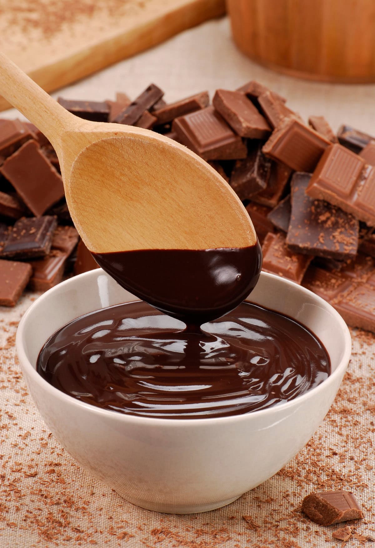 A bowl of melted chocolate with a wood spoon dripping chocolate.