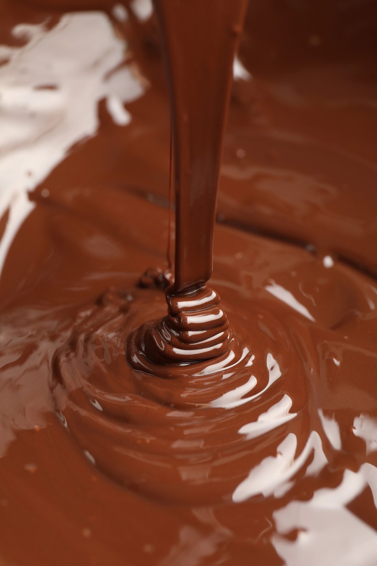 Melted chocolate dripping into a pot of melted chocolate.