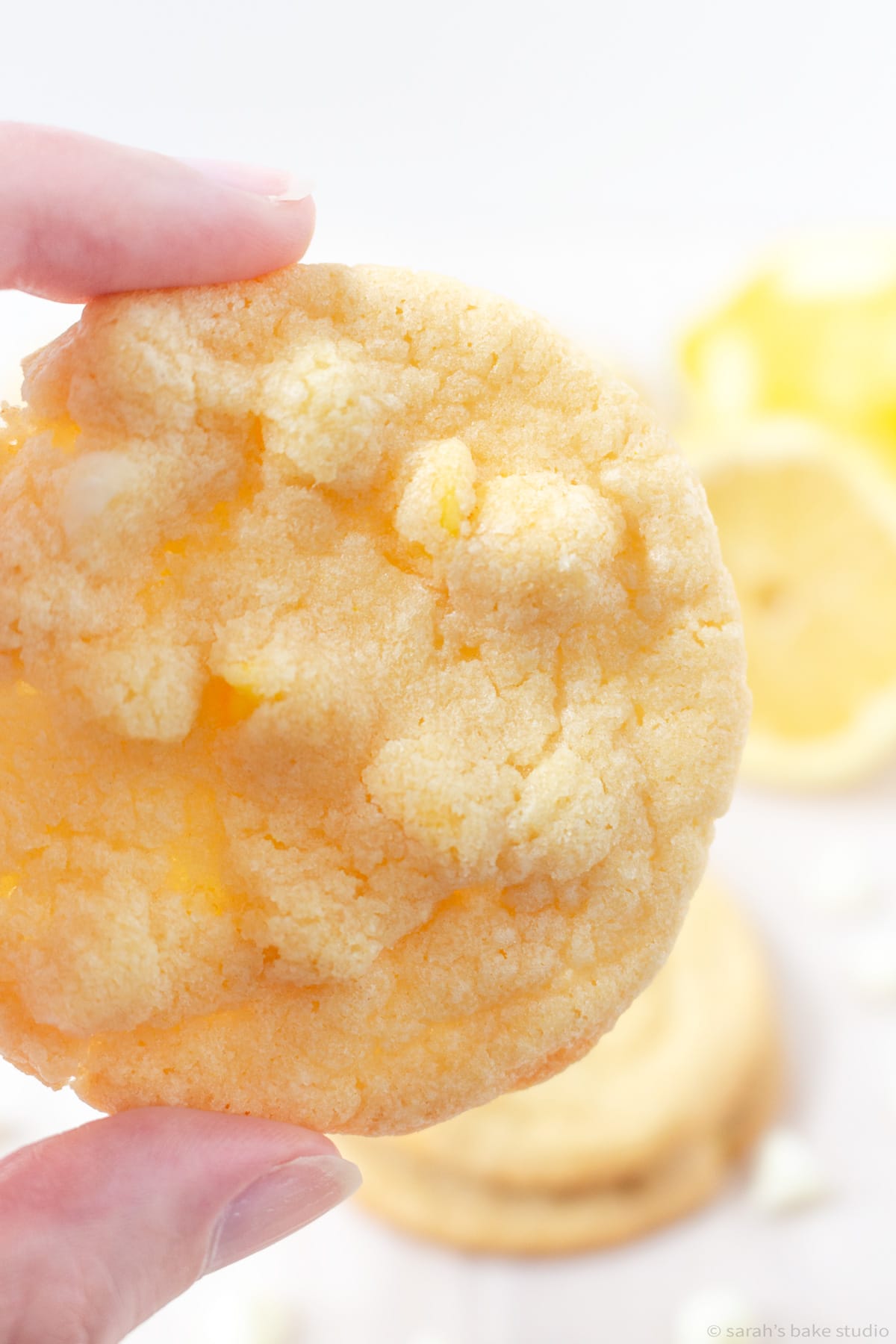 Two fingers holding a Lemon White Chocolate Chip Cookie.
