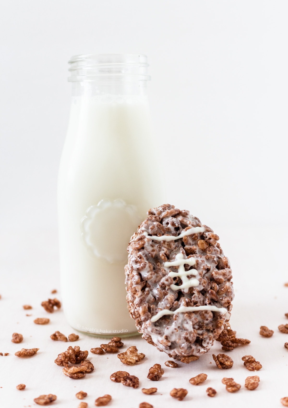 A glass bottle of milk with a Football Chocolate Rice Krispies Treat balancing against it.