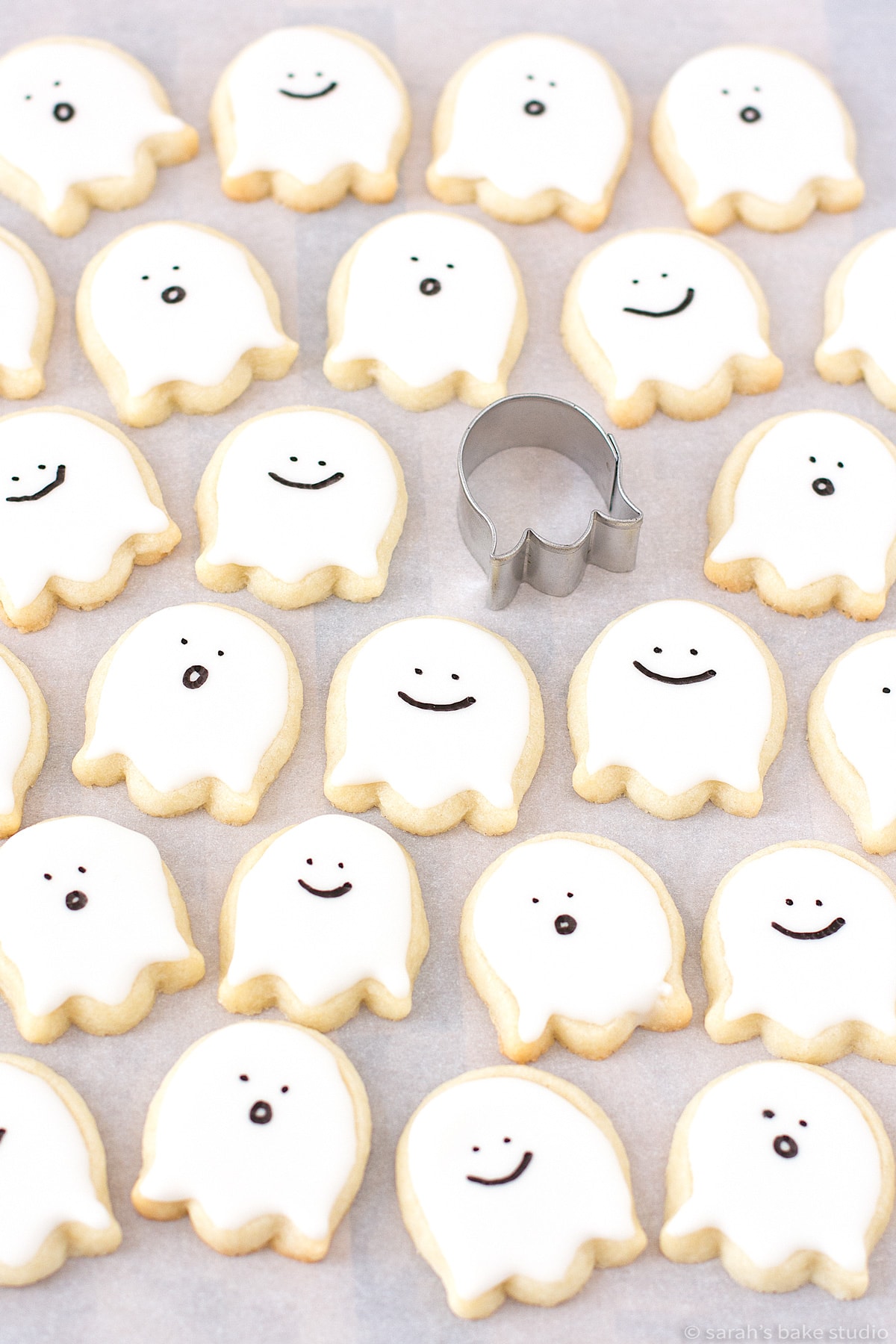 A flatlay of Happy Little Ghost Sugar Cookies with the cookie cutter used to make them.