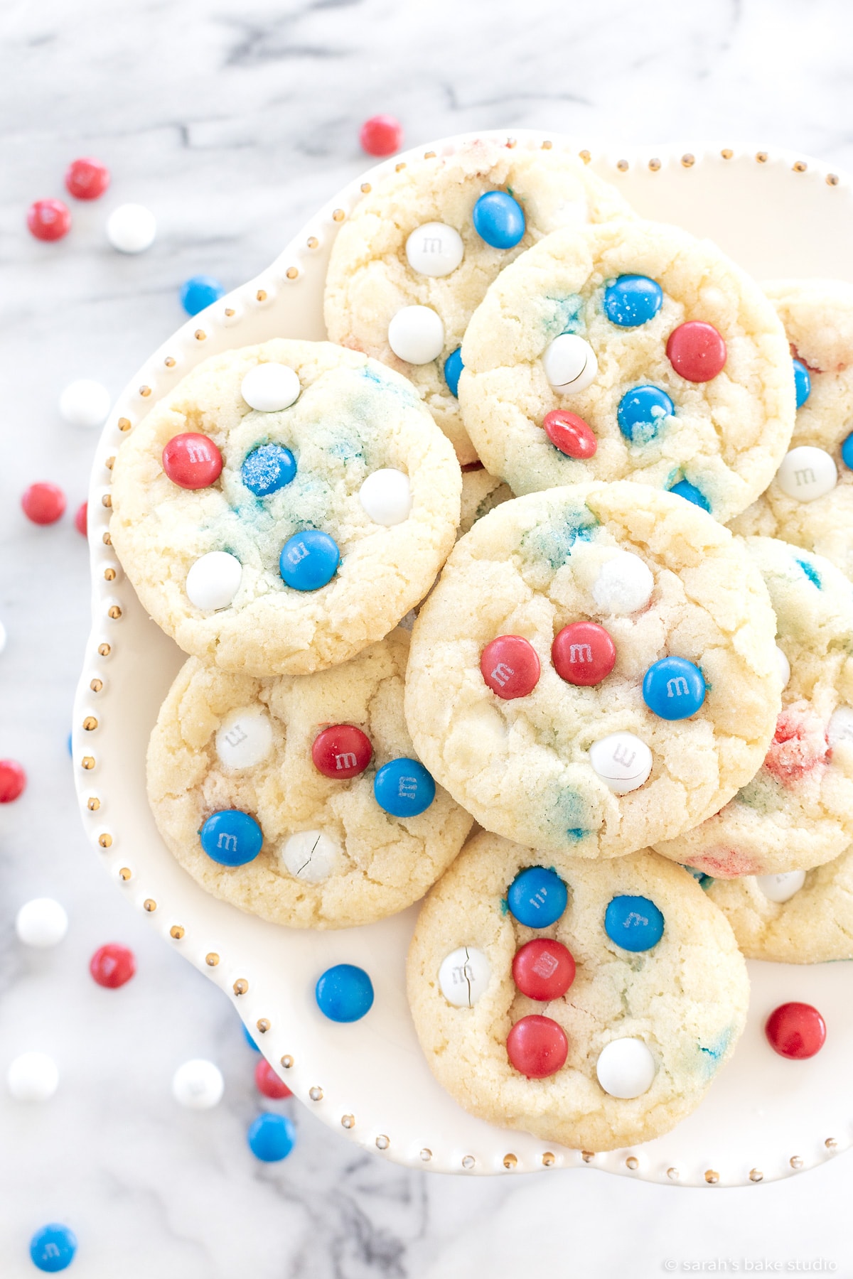 patriotic m&m cookies displayed on a white cake plate.