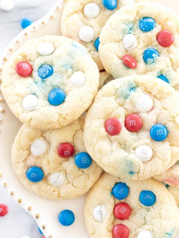 patriotic m&m cookies displayed on a white cake plate.