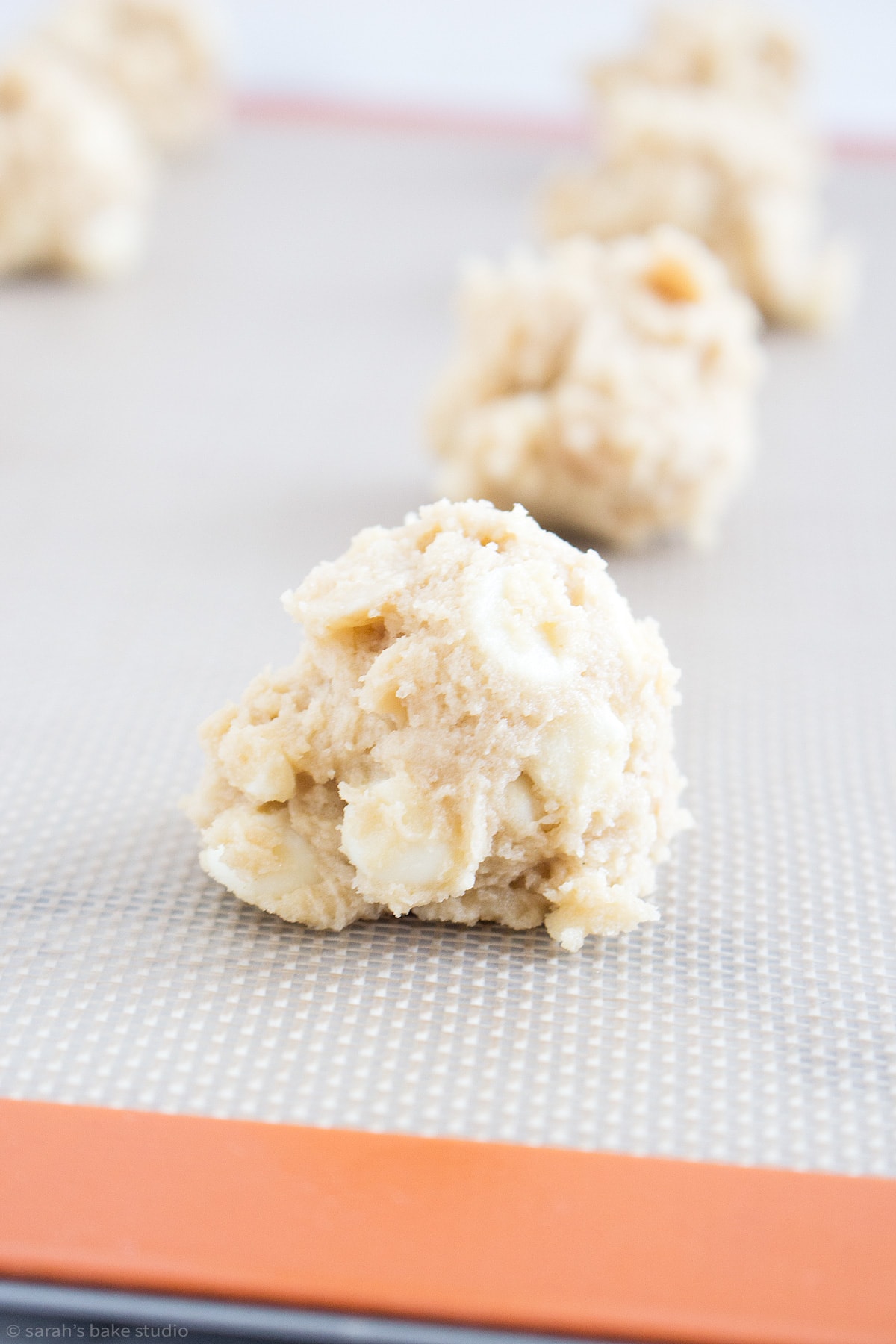 A scoop of White Chocolate Macadamia Nut cookie dough on a baking sheet.