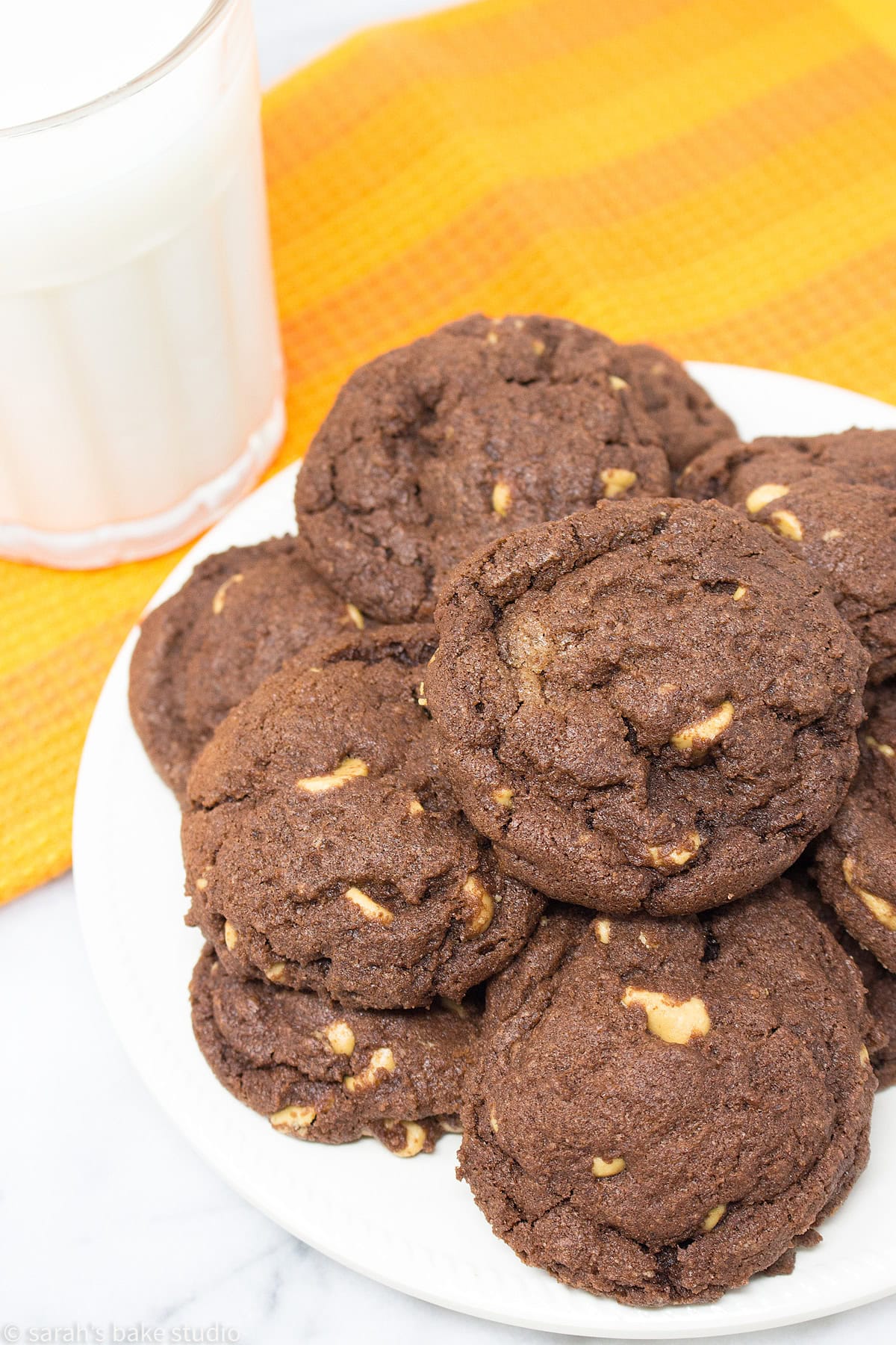 A plate stacked with Chocolate Peanut Butter Chip Cookies and a glass of milk.