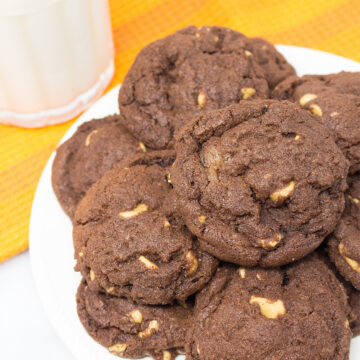 A plate stacked with Chocolate Peanut Butter Chip Cookies and a glass of milk.