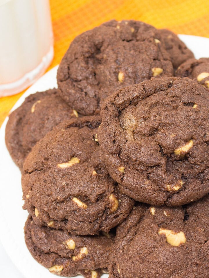 A plate stacked with Chocolate Peanut Butter Chip Cookies and a glass of milk.