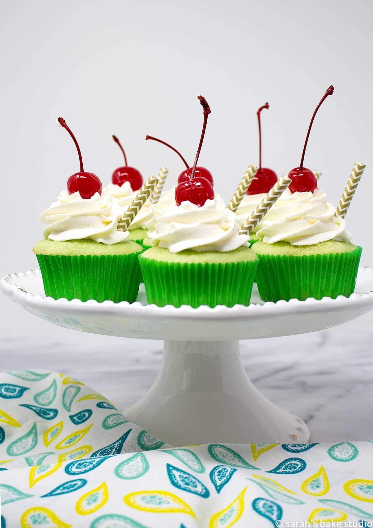 a white cake plate stacked with shamrock shake cupcakes and sitting on a tea towel.