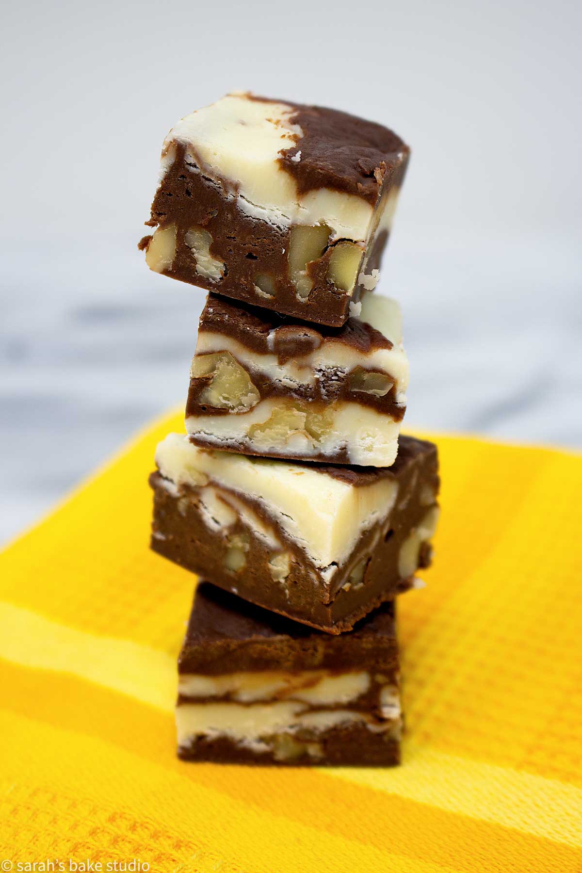 marble walnut fudge stacked into a tower sitting on a yellow tea towel.