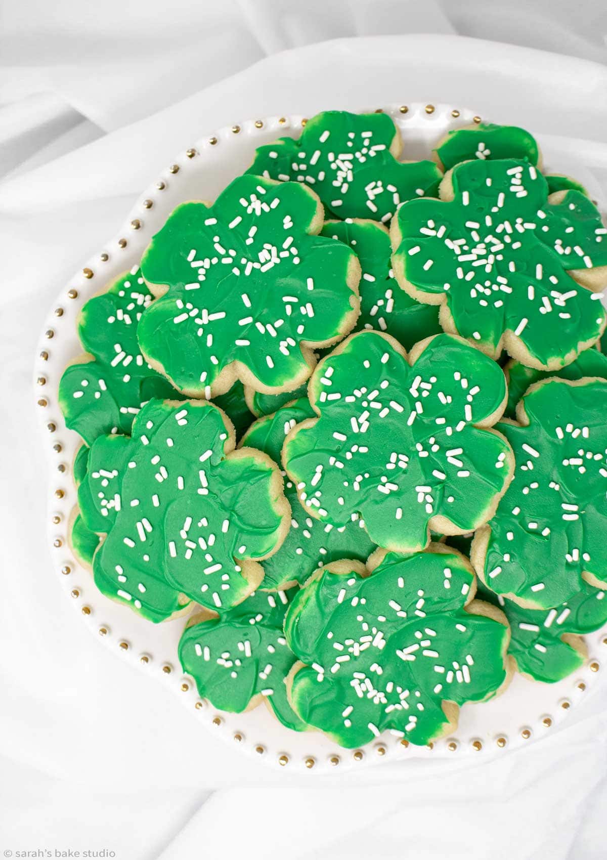 a white cake plate stacked with four-leaf clover decorated cookies.