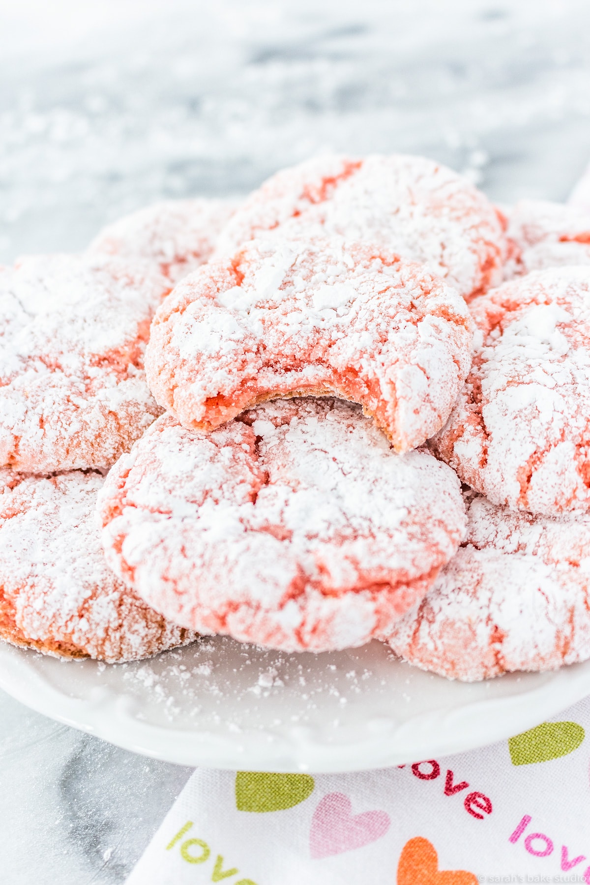 a plate piled with strawberry crinkle cookies; the top cookie has a bite out of it.