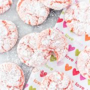 a valentines day tea towel with strawberry crinkle cookies on top; one of the cookies has a bite out of it.