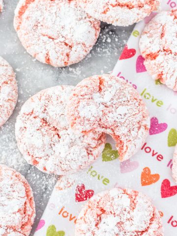 a valentines day tea towel with strawberry crinkle cookies on top; one of the cookies has a bite out of it.