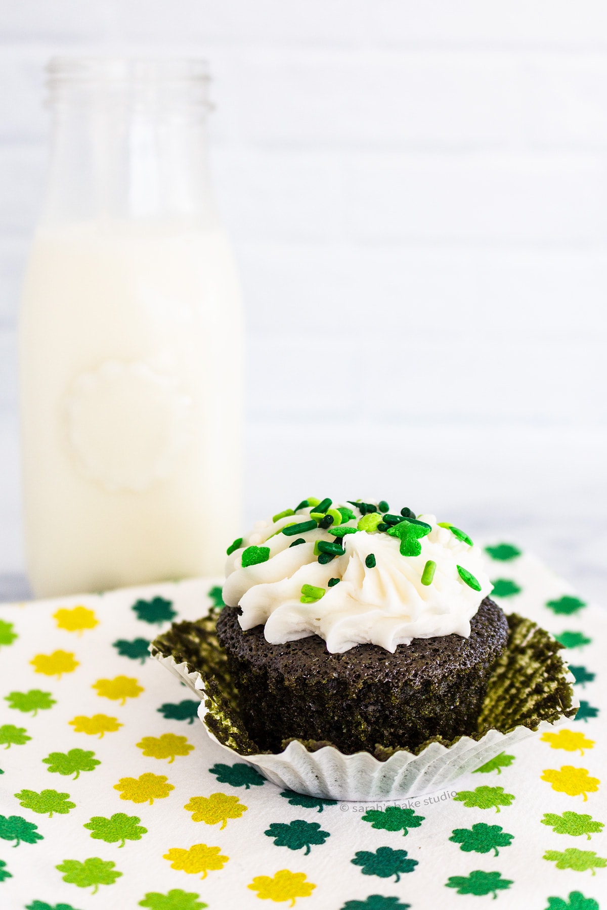 A bottle of milk with a semi-unwrapped Green Velvet Cupcake sitting in front of it.