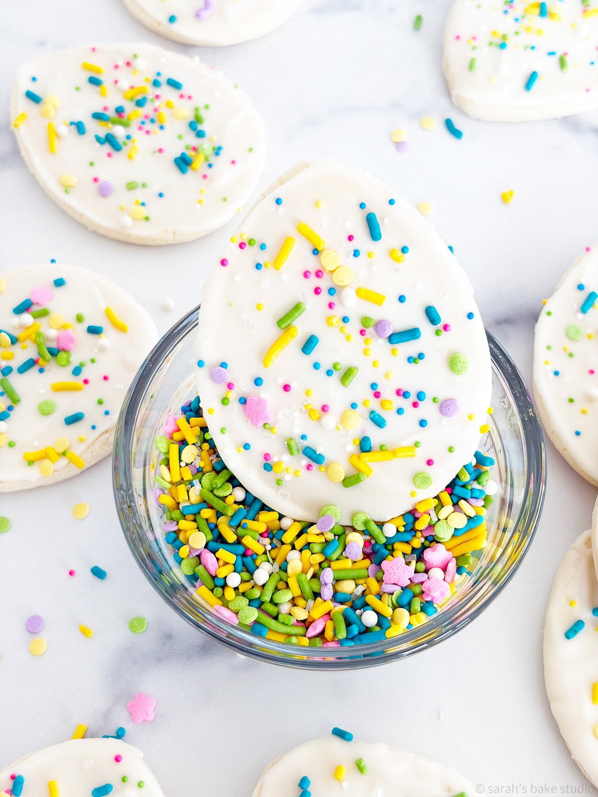 A bowl of spring sprinkles with a White Chocolate Easter Egg Sugar Cookie sitting inside.